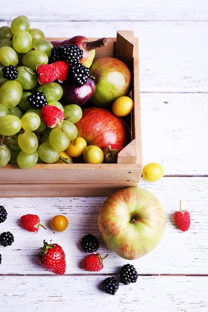 Différentes baies et fruits en boîte sur une table en bois libre