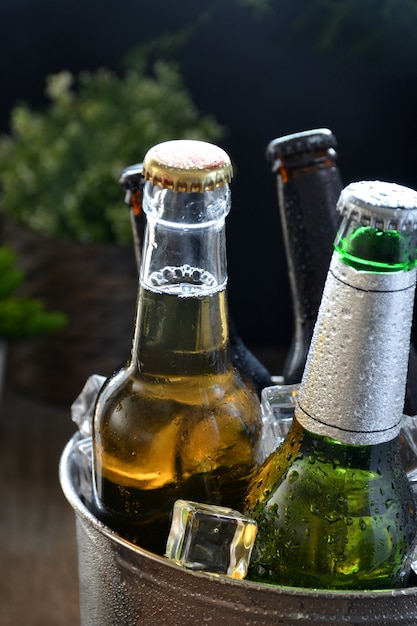 Différentes bières sur une table de bois. Il y a une bouteille et un verre avec de la glace pour les garder au froid