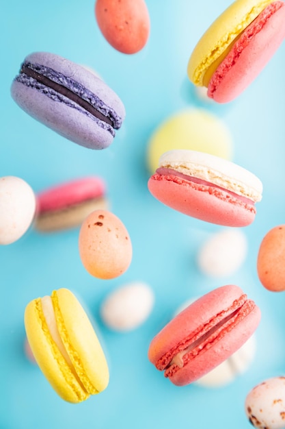 Différentes couleurs macarons volants et œufs en chocolat congelés dans l'air sur fond bleu flou vue de dessus gros plan