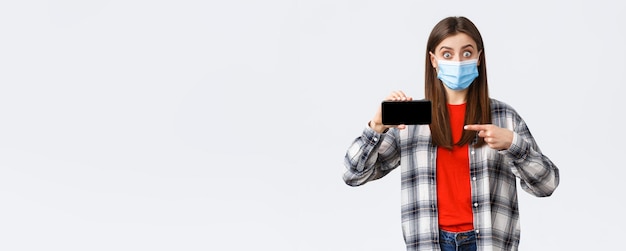 Différentes émotions covid19 distanciation sociale et concept technologique Une fille impressionnée et surprise dans un masque médical regarde étonné pointant du doigt l'écran du téléphone mobile