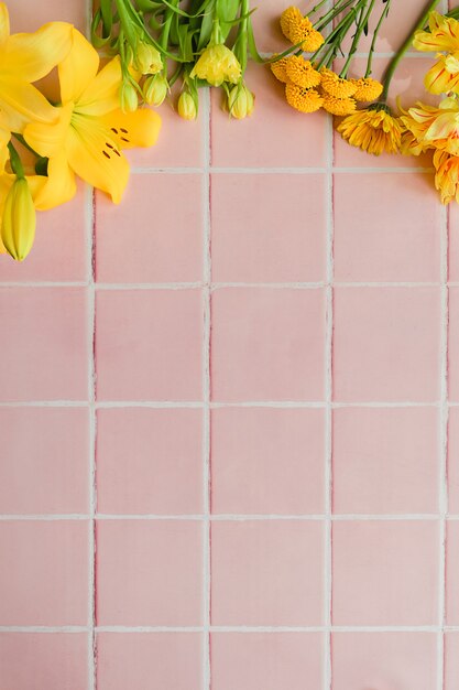 Différentes fleurs jaunes sur fond de carrelage rose