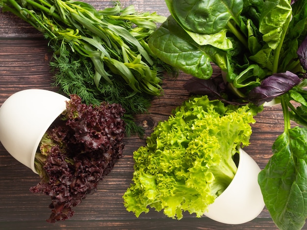 Différentes herbes fraîches comestibles, verts de vert et violet dans des pots blancs et sur une table en bois, vue du dessus,