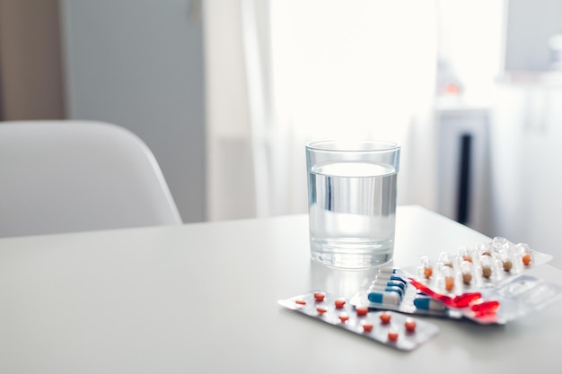 Différentes pilules et verre d'eau sur la table de la cuisine Santé et médecine