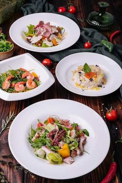 Différentes salades dans des assiettes blanches sur une table en bois