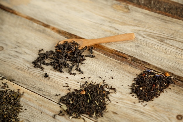 Différentes variétés de thé naturel sur une cuillère en bambou sur un fond en bois