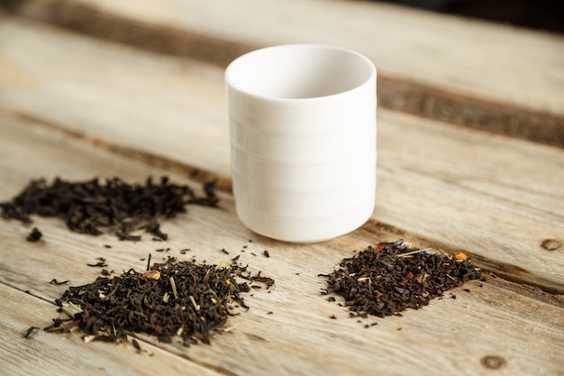 Différentes variétés de thé naturel sur une cuillère et brassées dans un verre sur un fond en bois.