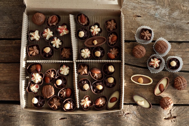 Différents bonbons au chocolat dans une boîte en papier sur fond de bois, gros plan