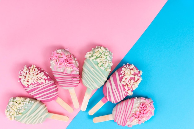 Différents cake pops sous forme de popsicle sur bâton sur fond rose et bleu Vue de dessus