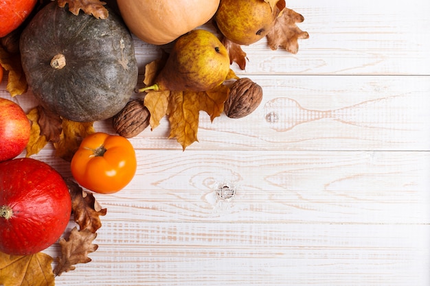 Différents légumes, citrouilles, pommes, poires, noix, tomates et feuilles sèches sur un fond en bois blanc. Humeur d'automne, surface. Récolte .