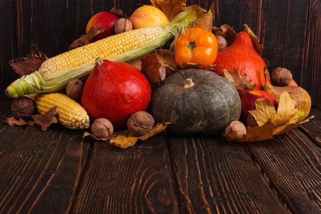 Différents légumes, citrouilles, pommes, poires, noix, tomates, maïs, feuilles jaunes sèches sur fond en bois. Humeur d'automne, surface. Récolte .