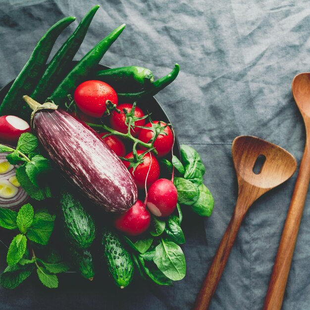 Différents légumes colorés frais dans une assiette sur une table avec des ustensiles de cuisine en bois