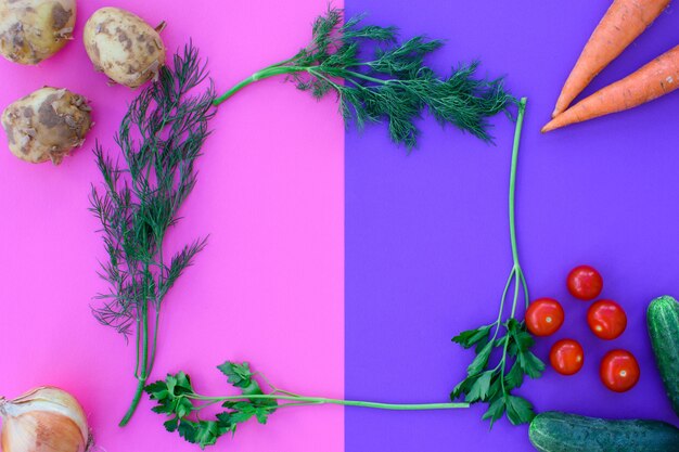 Différents légumes sur un double fond - rose et violet, légumes - pommes de terre, carottes, oignons, tomates, concombres et légumes verts. Régime équilibré.