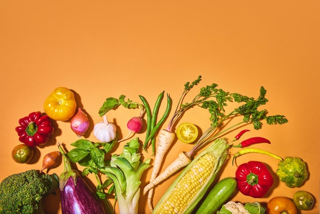 Différents légumes sur fond orange citrouille ail brocoli oignon maïs radis tomate