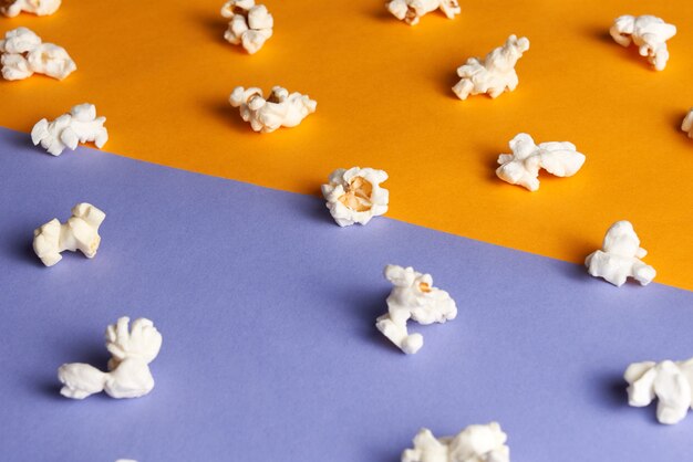 Différents morceaux de pop-corn savoureux sur demi-orange demi-violette. Concept de film.