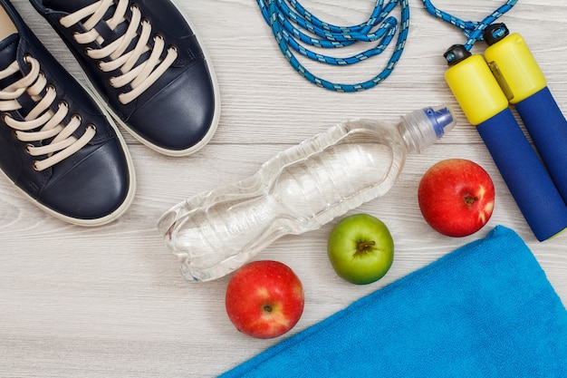 Différents outils de remise en forme avec bouteille d'eau et pommes dans la chambre ou la salle de sport sur sol gris