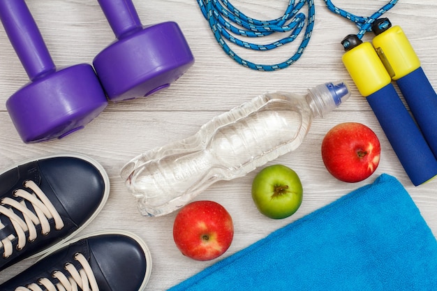 Différents outils de remise en forme avec bouteille d'eau et pommes dans la chambre ou la salle de sport sur sol gris