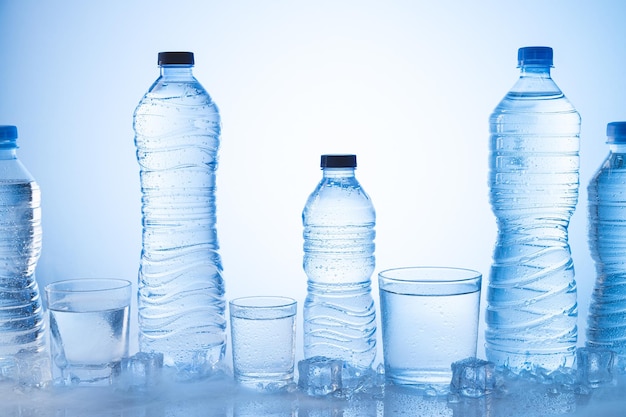 Différents types de bouteille d'eau minérale glacée avec des verres d'eau sur fond bleu