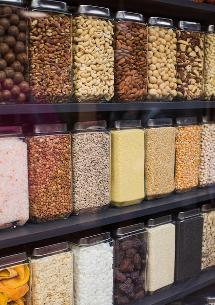 Différents types de céréales de noix et de fruits secs debout dans des bocaux sur l'étagère du magasin