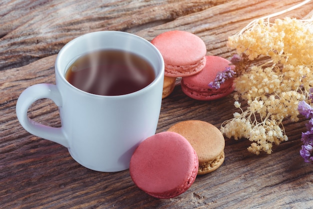 Différents types de couleur des macarons avec une tasse de thé chaud sur le vieux fond en bois de grunge