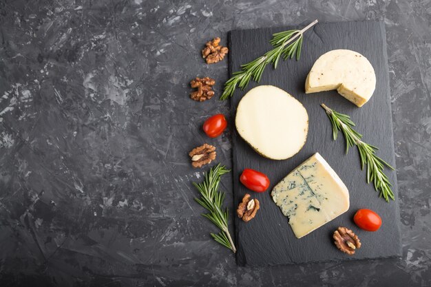 Différents types de fromage au romarin et tomates sur ardoise noire sur un béton noir