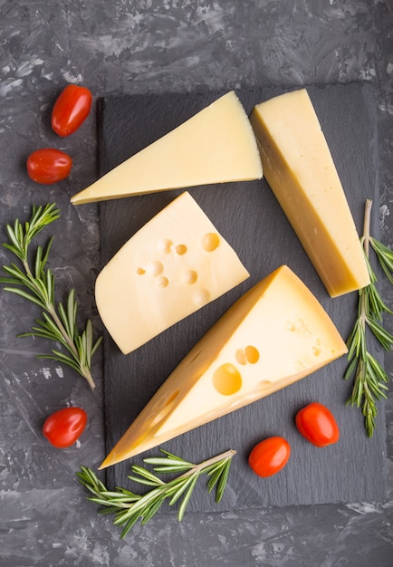 Différents types de fromage au romarin et tomates sur ardoise noire sur une surface de béton noir