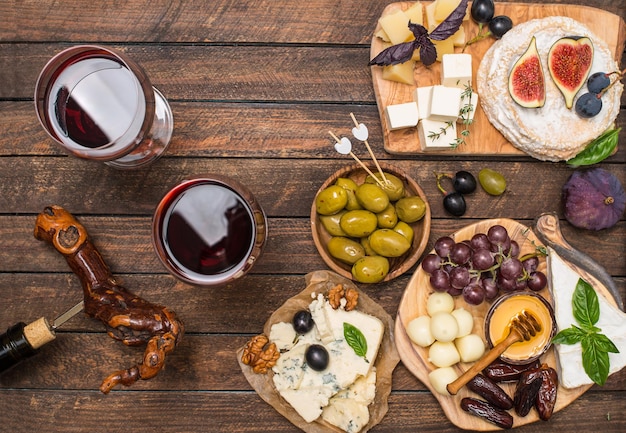 Différents types de fromage raisins dates olives noix figue et vin sur fond de bois