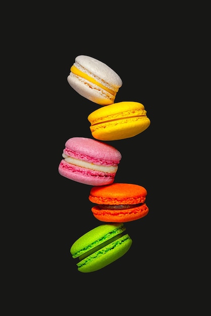 Différents types de macarons en mouvement tombant sur fond noir Macarons sucrés et colorés