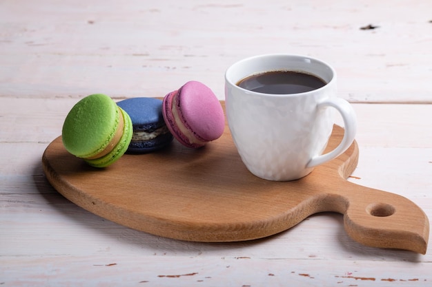 Différents types de macarons et une tasse de café blanche sur une planche de bois
