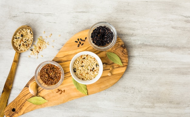 Différents types de riz dans des bols sur une planche en bois avec une cuillère