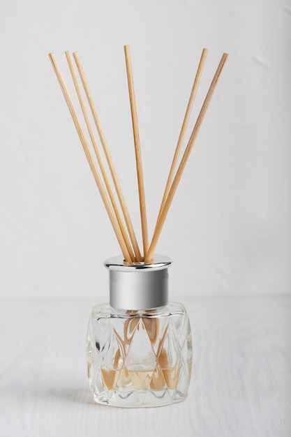 Diffuseur de parfum de maison avec des bâtons en bois dans une élégante bouteille en verre sur une table en bois blanc