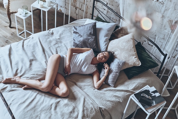 Dimanche matin sans soucis. Vue de dessus de la belle jeune femme gardant les yeux fermés et souriant