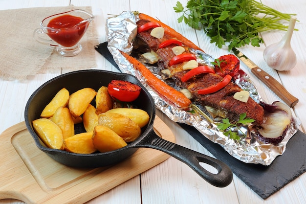 Dîner campagnard - côtelettes de veau rôties avec légumes et pommes de terre sur une table en bois blanc