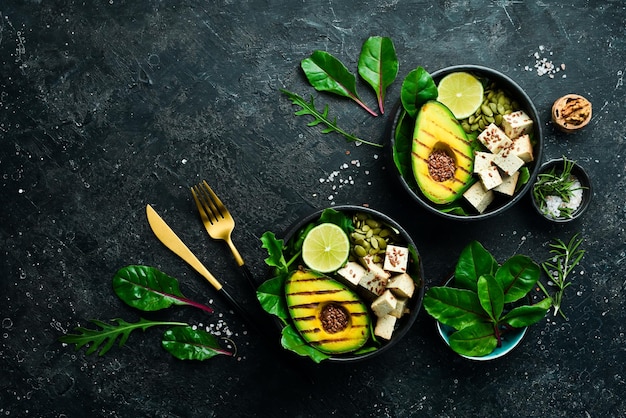 Dîner ou déjeuner sain Nourriture végétarienne dans un bol avocat tofu fromage lin graines de citrouille et épinards Le concept d'une alimentation saine Sur un fond de pierre noire Vue de dessus