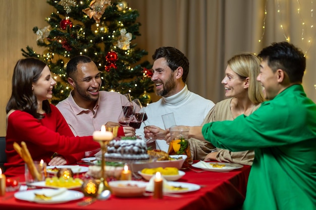 Dîner festif de noël divers amis célébrant le nouvel an à la maison manger et boire du vin