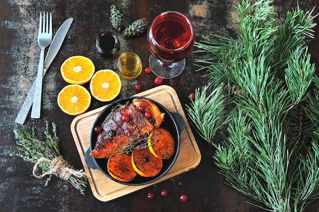 Dîner de Noël. Poitrine de poulet cuite au four avec mandarines et canneberges. Branches d'arbres de Noël et un verre de vin.