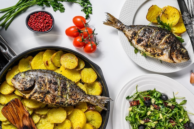 Dîner avec poisson dorade grillé, salade de roquette aux tomates, pommes de terre au four. Fond blanc. vue de dessus