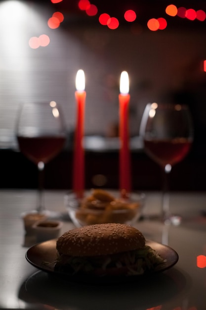 Dîner romantique deux verres de vin et des pépites de hamburger aux chandelles sont dans le noir avec les lumières du nouvel an à l'arrière-plan