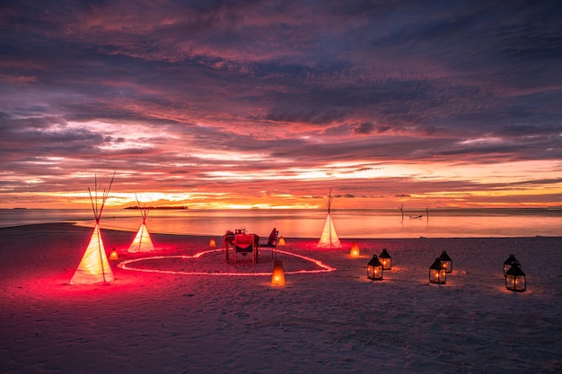 Dîner romantique sur la plage au coucher du soleil. Anniversaire, repas de destination de lune de miel, bougies allumées