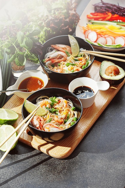 Dîner romantique pour deux nouilles de riz de cuisine asiatique avec crevettes et fruits de mer pois verts et oignons sauce soja et divers légumes frais dîner romantique dans des assiettes noires avec des baguettes japonaises