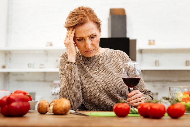 Dîner sain. Belle dame bouleversée aux cheveux attachés portant un pull beige chaud et buvant du vin seul