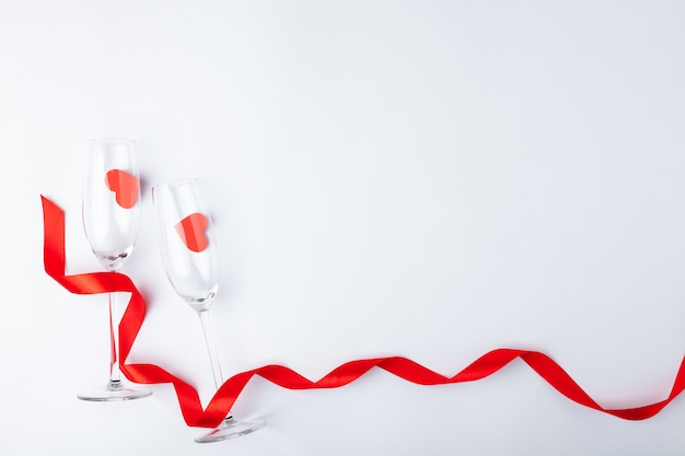 Dîner de Saint Valentin romantique cadre festif, ruban rouge, verre de champagne, bouteille, coeurs sur fond en bois blanc. Copiez l'espace, placez le texte. Vue de dessus.