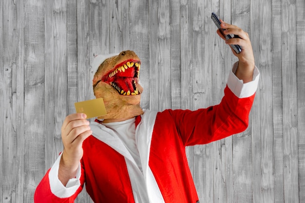 Dinosaure déguisé en Père Noël avec carte de crédit et téléphone portable en main