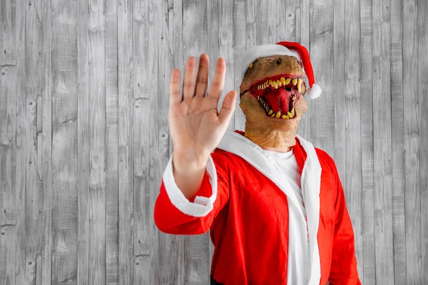 Dinosaure habillé en Père Noël avec sa main faisant le geste d'arrêt.