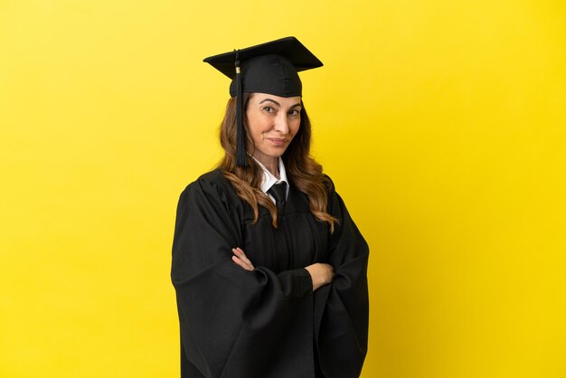 Diplômé de l'université d'âge moyen isolé sur fond jaune avec les bras croisés et impatient