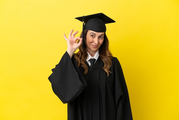 Diplômé de l'université d'âge moyen isolé sur fond jaune montrant un signe ok avec les doigts