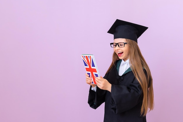 Un diplômé vêtu d'une robe noire et d'un chapeau carré regarde avec surprise un manuel d'anglais, un arrière-plan isolé.