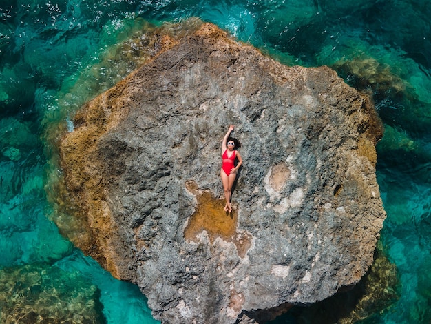 Directement au-dessus de la femme en maillot de bain rouge au rocher entouré par la mer vacances en grèce