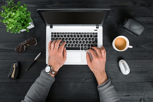 Directement au-dessus de la vue des mains humaines tapant sur un ordinateur portable. Ordinateur portable, tablette numérique, agenda, tasse à café et plante en pot sur le bureau. Homme travaillant à domicile.