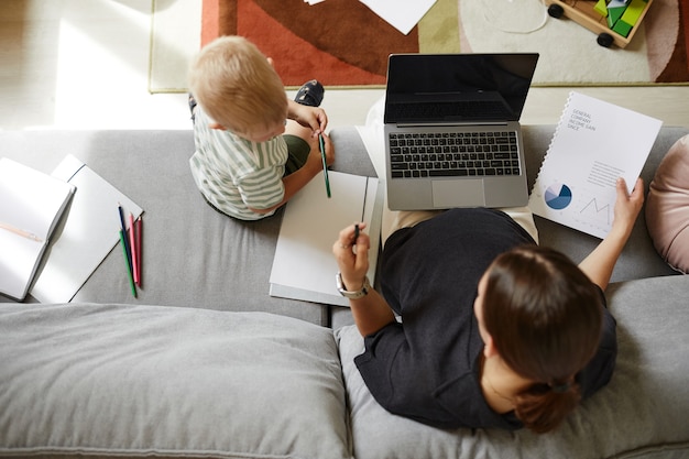 Directement au-dessus de la vue d'une mère enceinte assise avec un ordinateur portable sur les genoux et travaillant avec les finances pendant que son fils lui parle