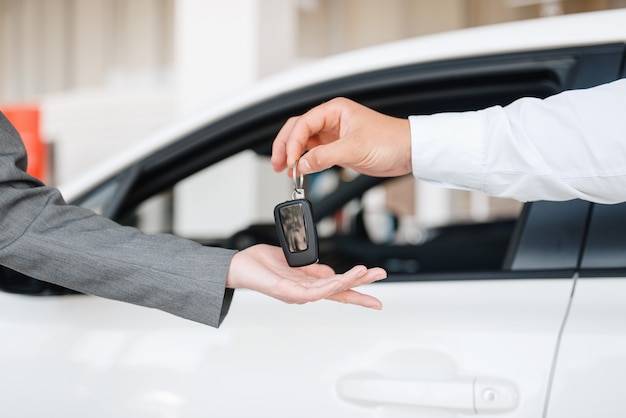 Le directeur donne à la femme la clé de la nouvelle voiture dans la salle d'exposition.